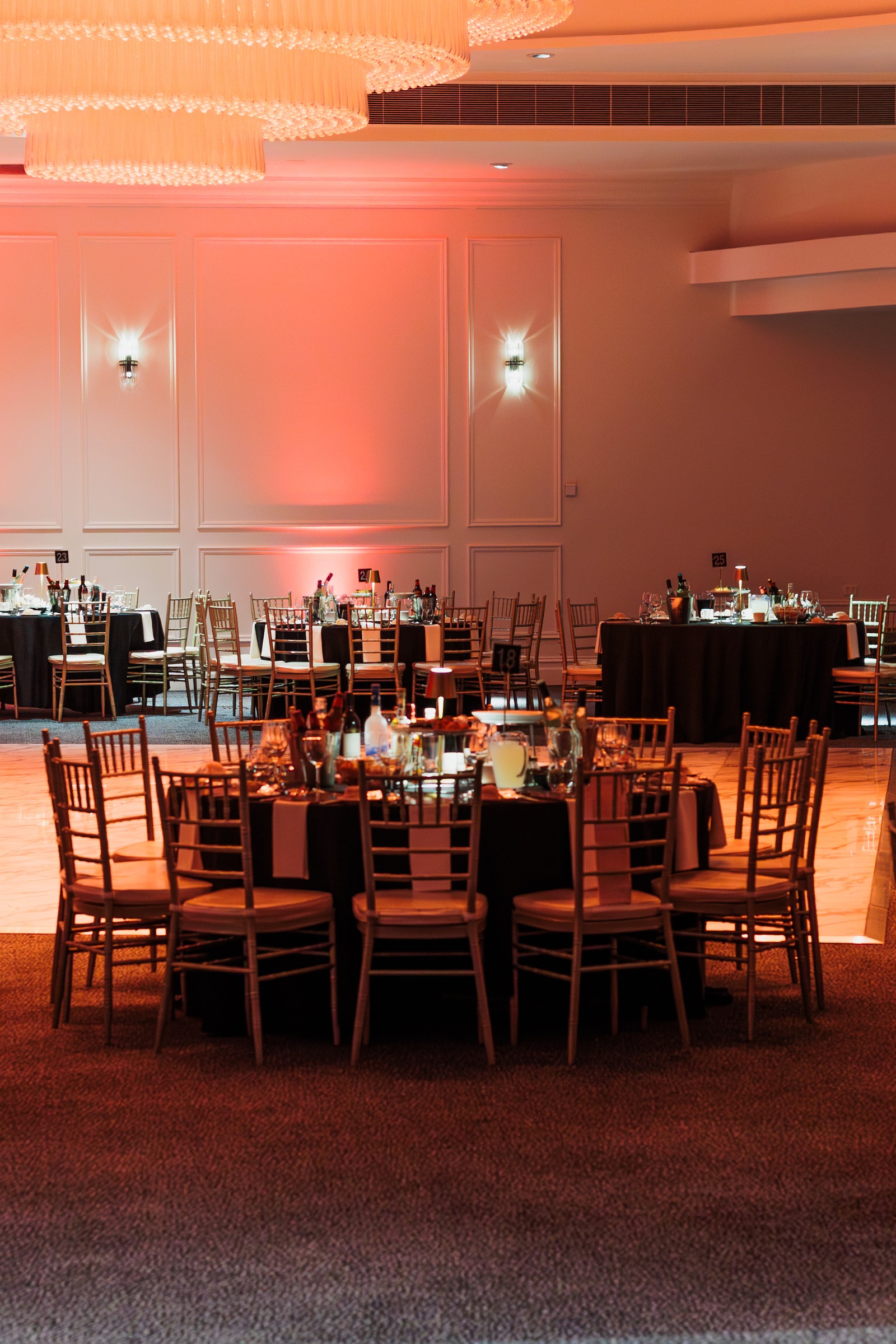 Melrose ballroom set with round tables and gold chairs under red uplighting