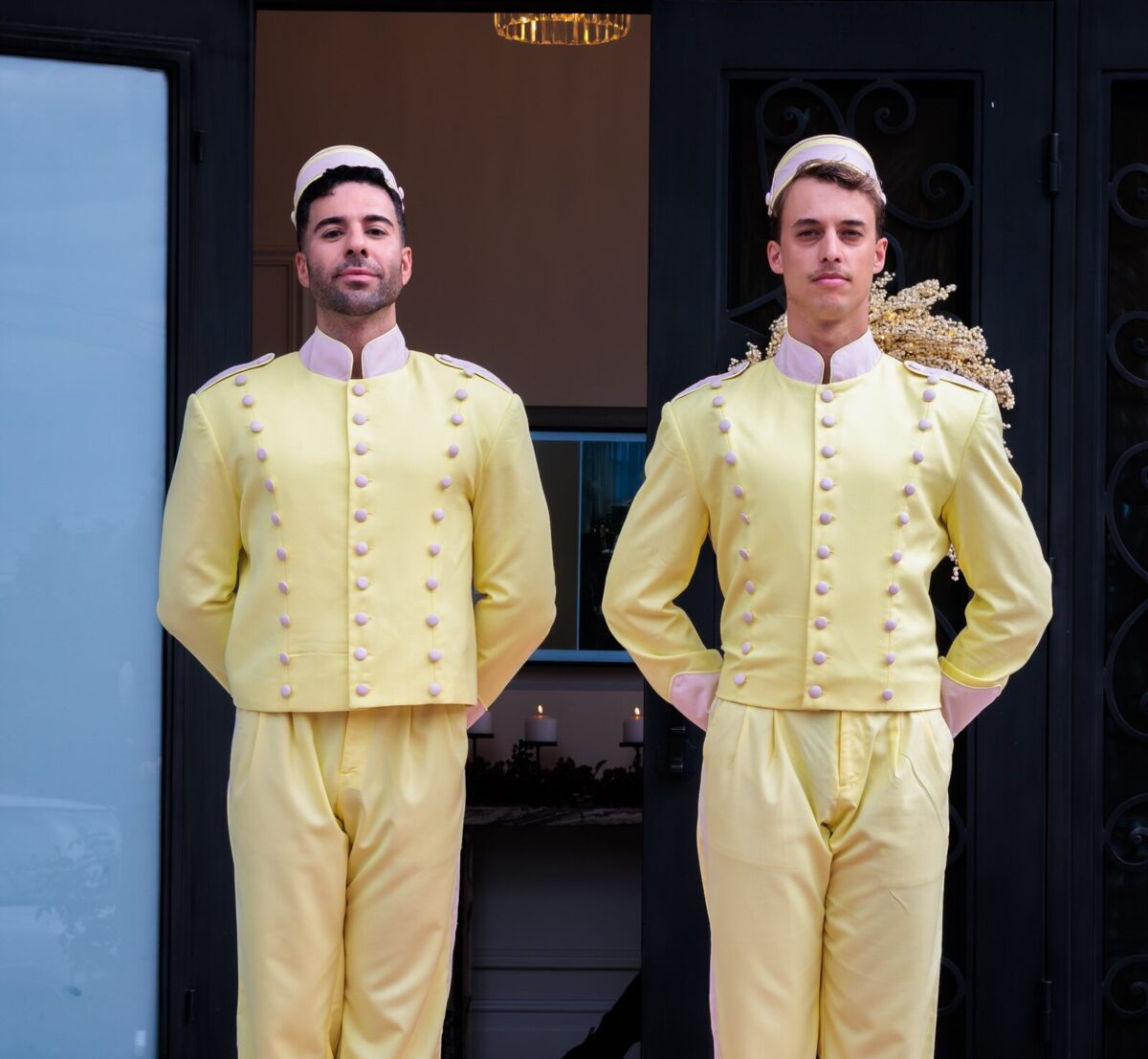 Two greeters in pastel yellow bellboy uniforms on the red carpet entrance