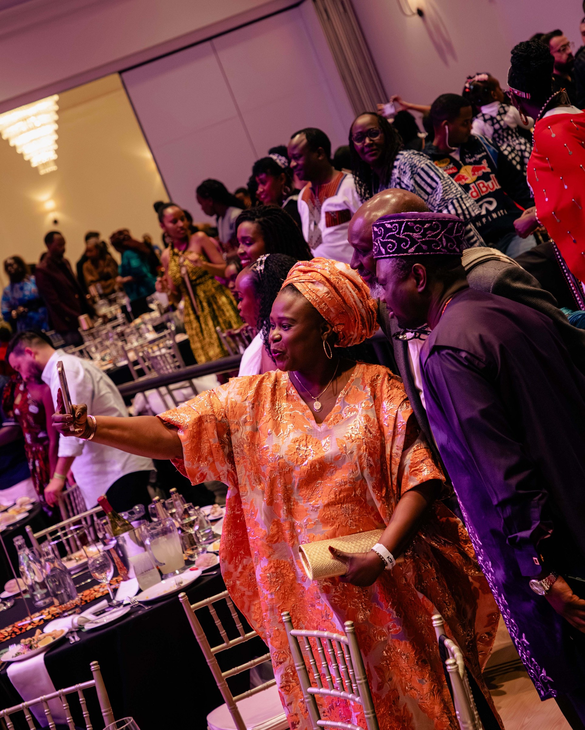 Guest in a vibrant orange gown dancing among tables at a cultural celebration