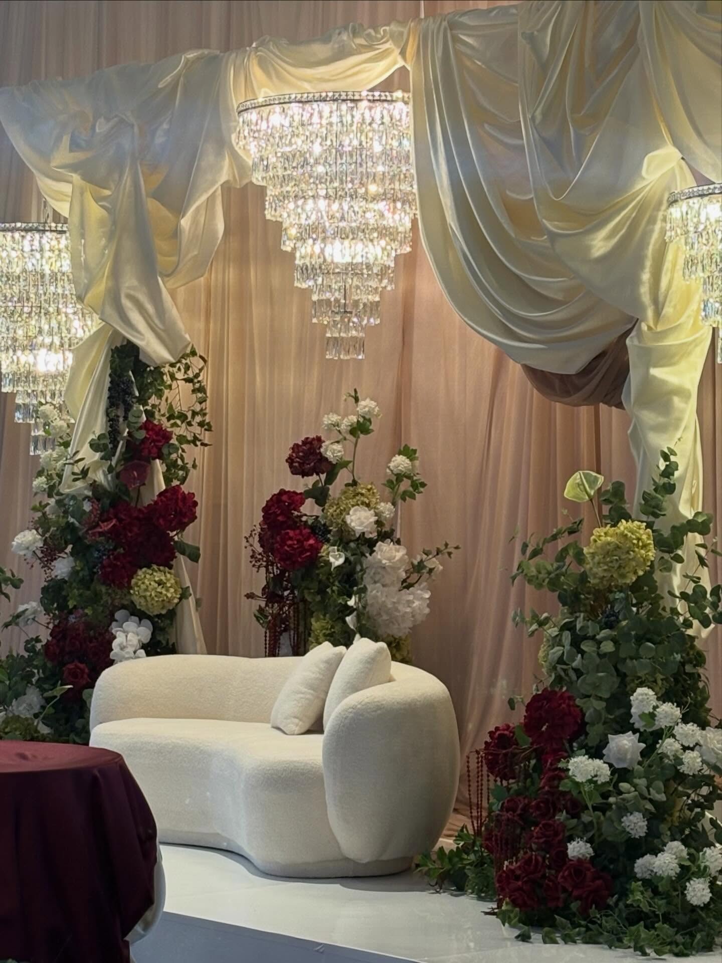 Draped stage with cream sofa and red and white florals for a cultural wedding at Melrose Events