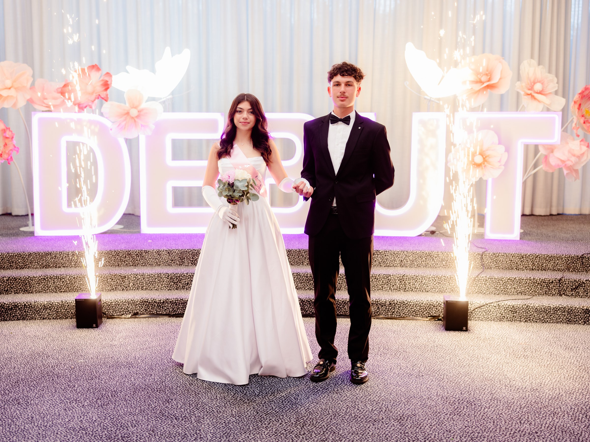 Debutante couple posing in front of the Debut sign with sparklers and pink florals