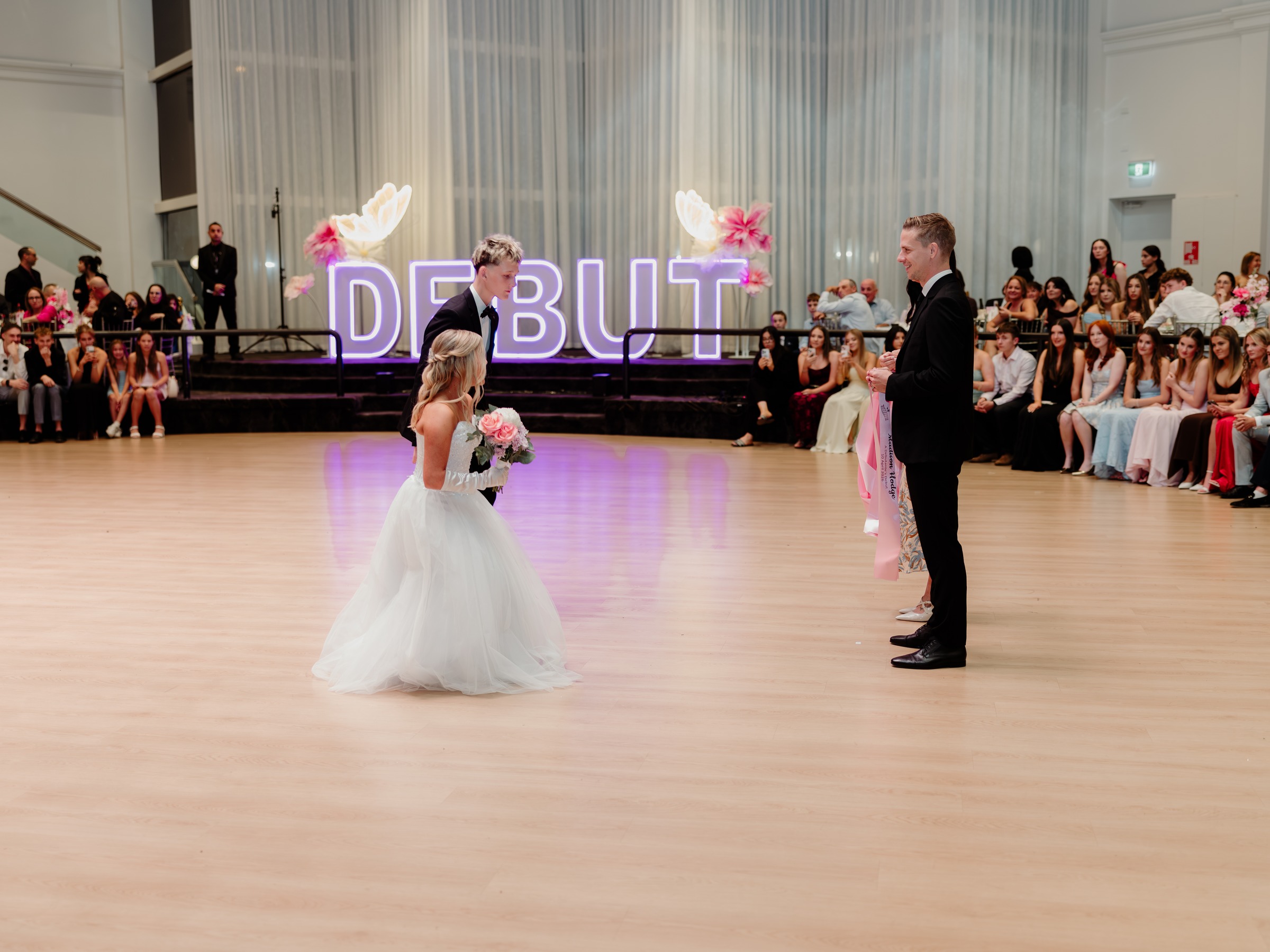 Debutante and her partner alone on the dance floor in front of the illuminated Debut sign at Melrose Events