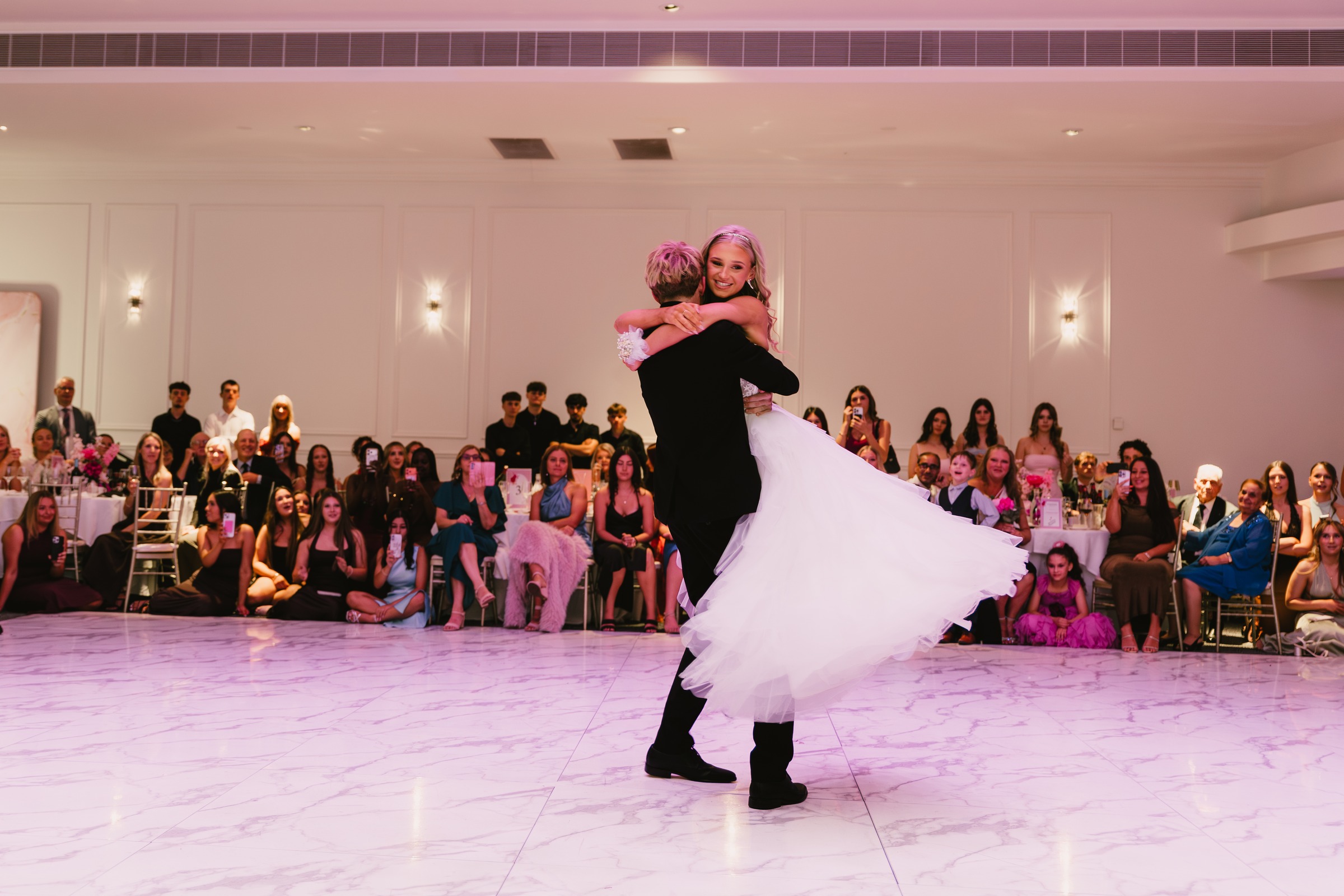 Debutante couple embracing on the dance floor under pink lighting