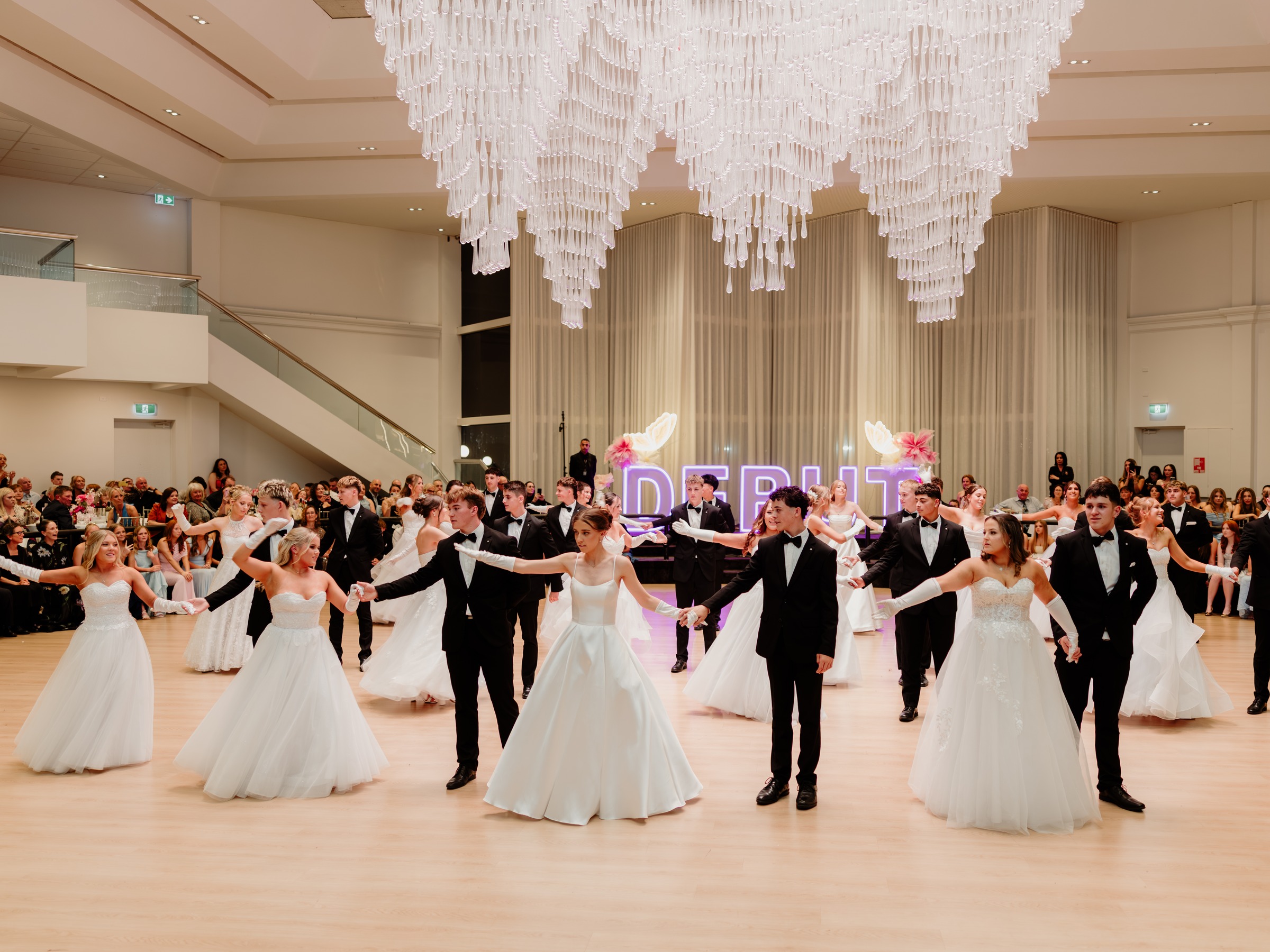 Debutante couples presented in a row beneath the chandelier in the Melrose Grand Ballroom
