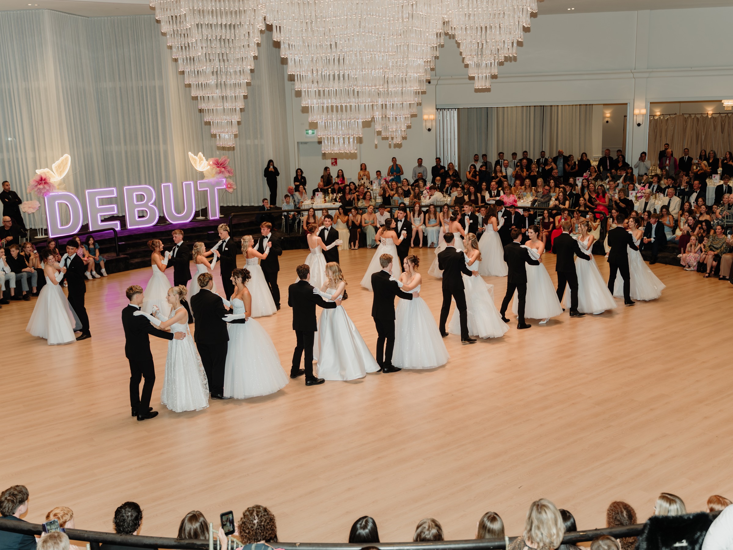 Debutante couples waltzing beneath the chandelier while families watch from their tables