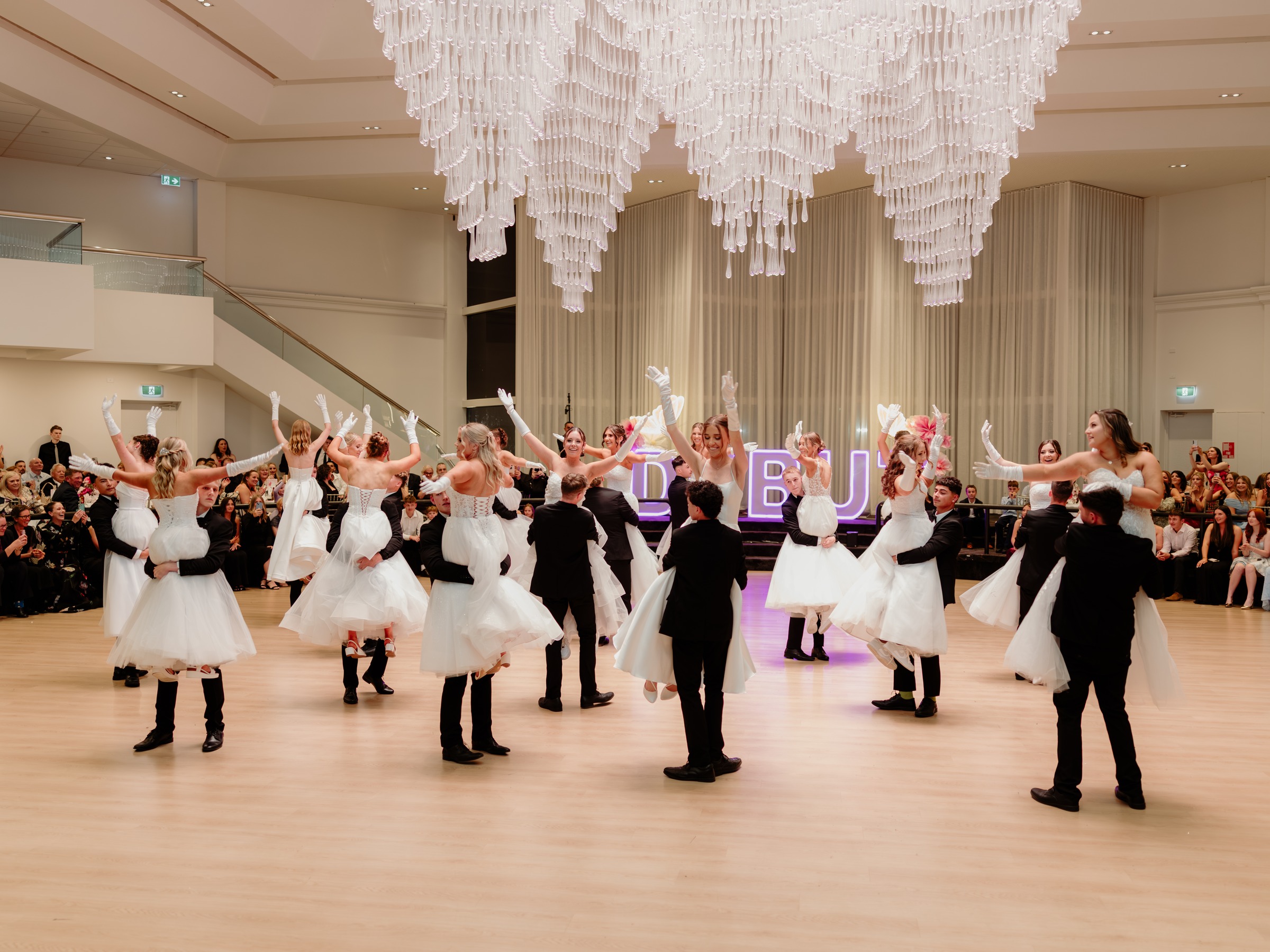 Debutante couples waltzing beneath the Grand Ballroom chandelier at a debutante ball at Melrose Events