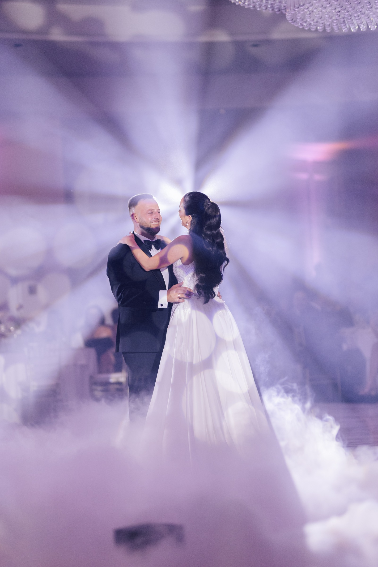 Bride and groom embracing during their first dance under purple lighting