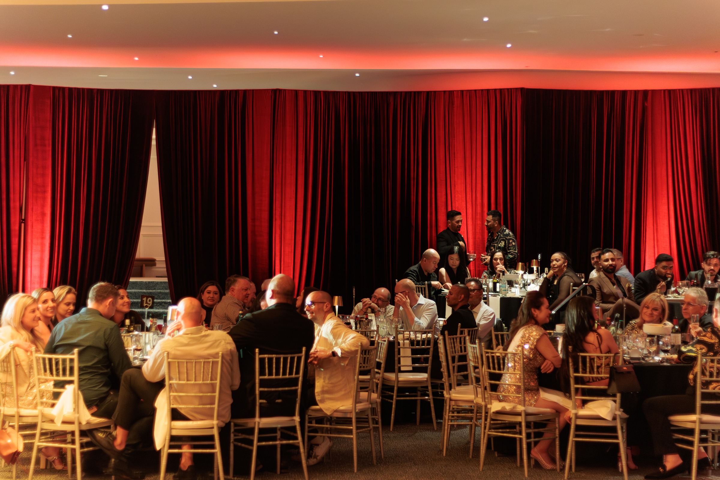 Gala dinner guests seated before a live band and red velvet stage curtain