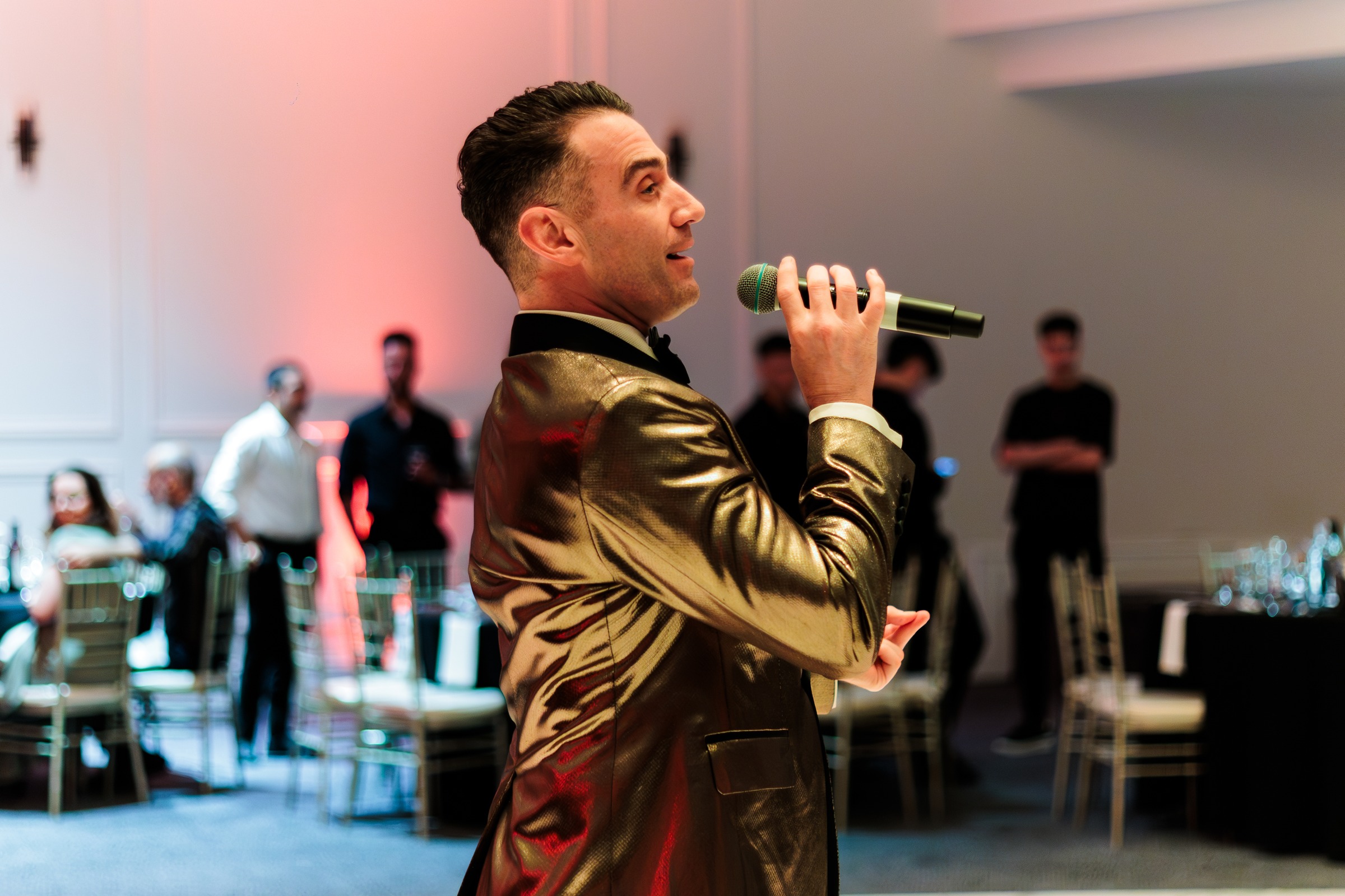 MC in a gold sequin jacket performing to guests on the ballroom floor