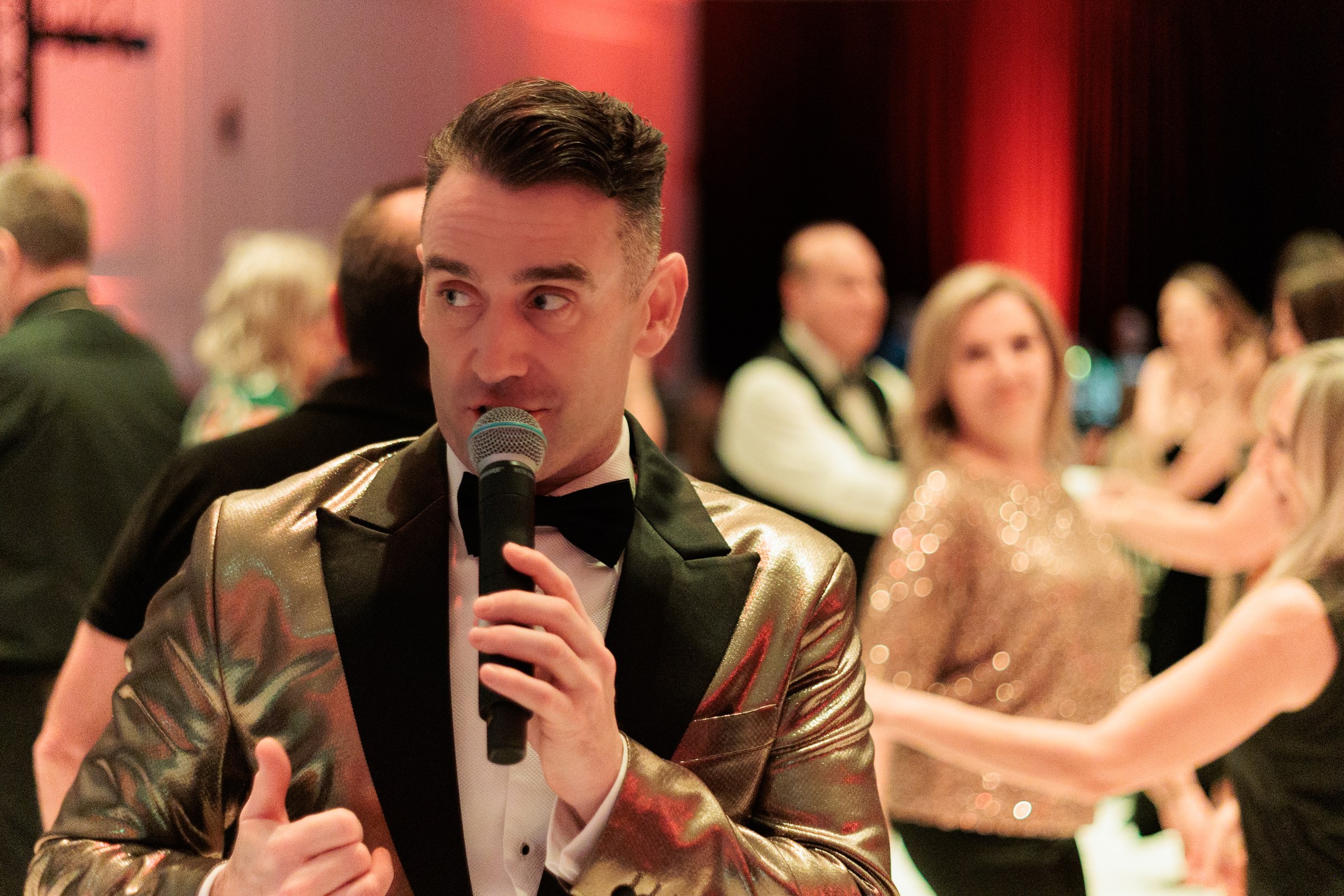 Entertainer in a gold jacket and bow tie among dancing guests