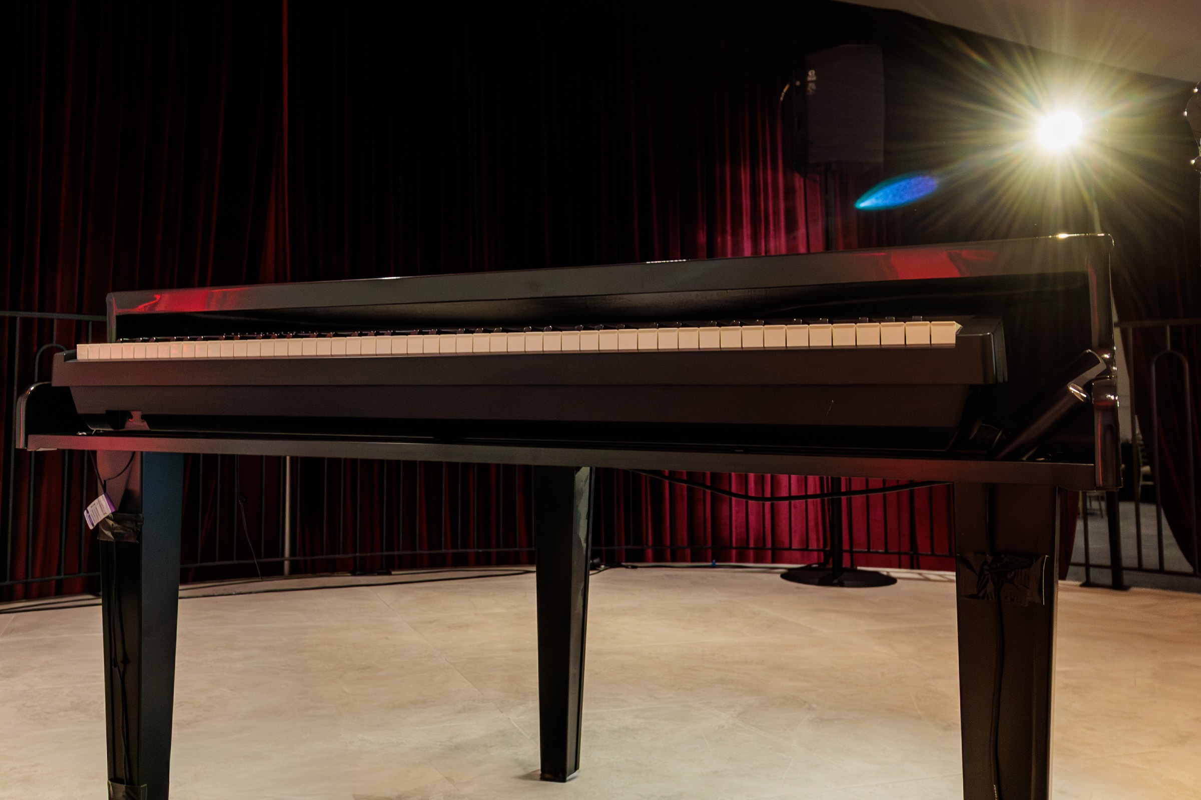 Grand piano on stage in front of red velvet drapes at Melrose Events