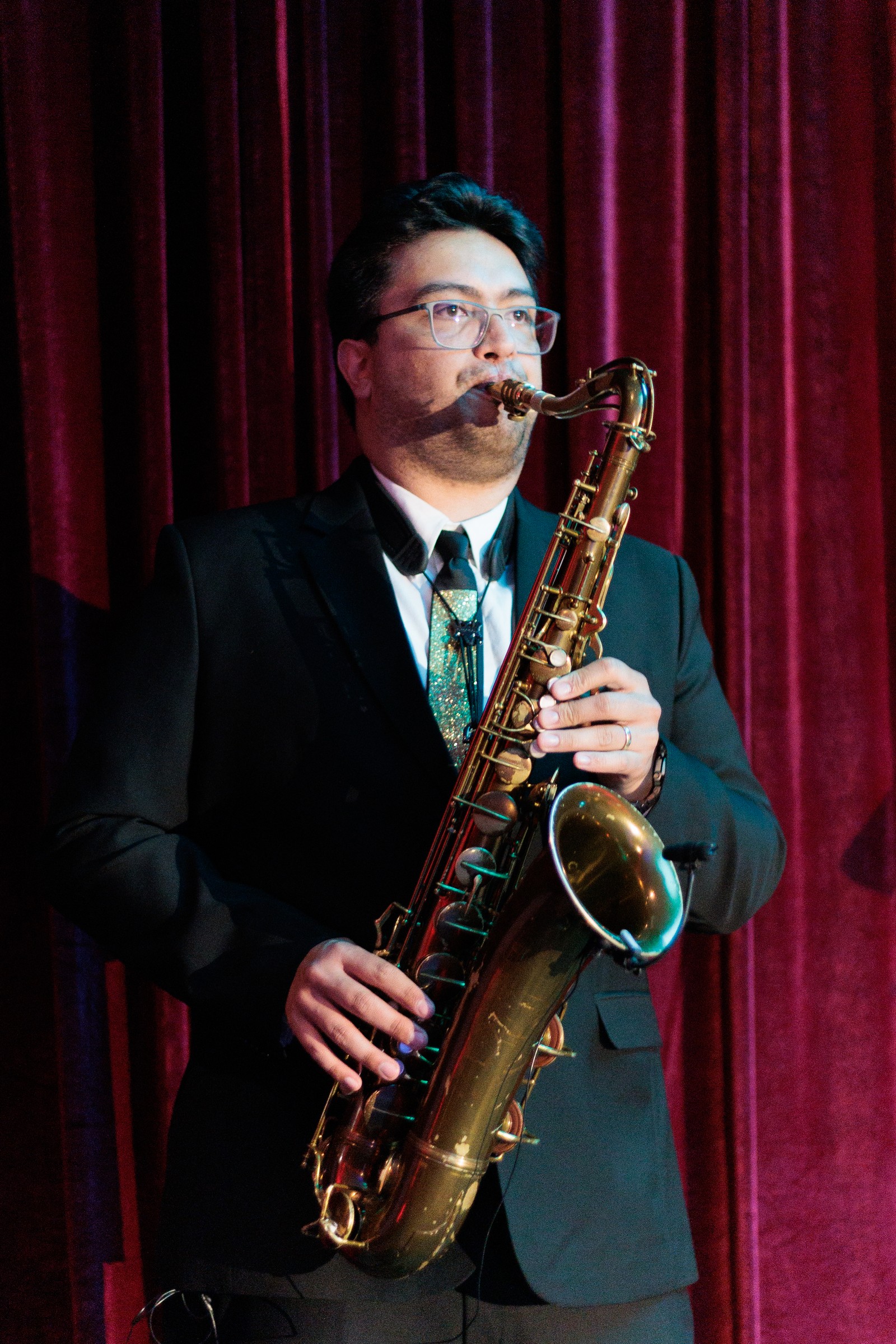 Saxophonist performing on stage in front of red drapes at Melrose