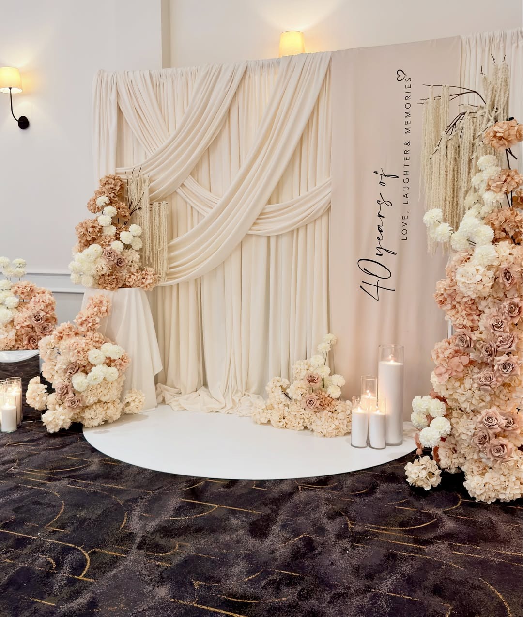 Draped backdrop with cream florals, candles and a 40 years of love neon sign for an anniversary celebration at Melrose Events