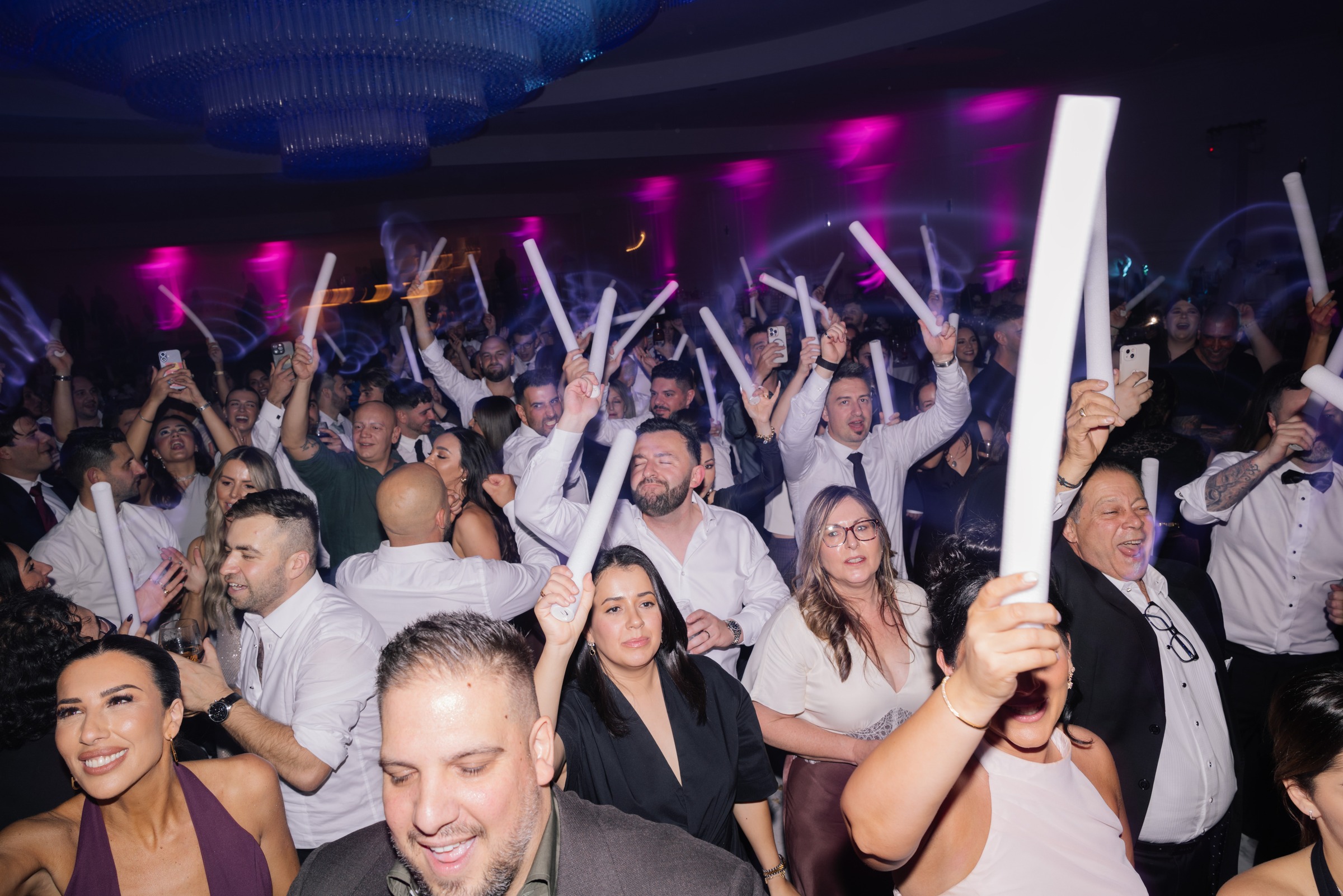 Wedding guests celebrating on a packed dance floor with light-up batons